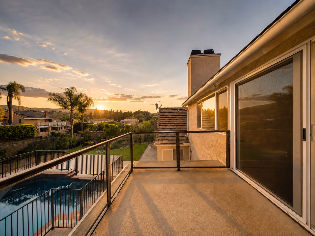 Sunlit balcony of a senior living exterior with pool and palm trees at sunset.