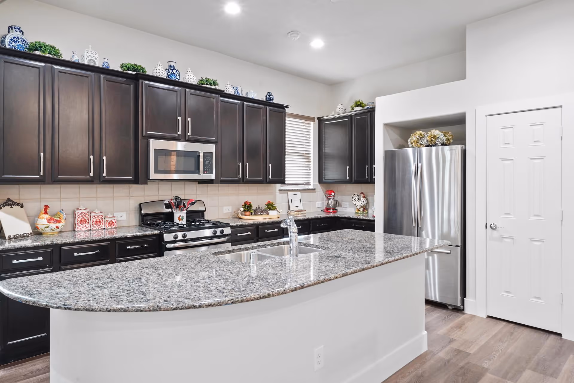 Modern kitchen with dark cabinets, granite island, and stainless steel appliances.