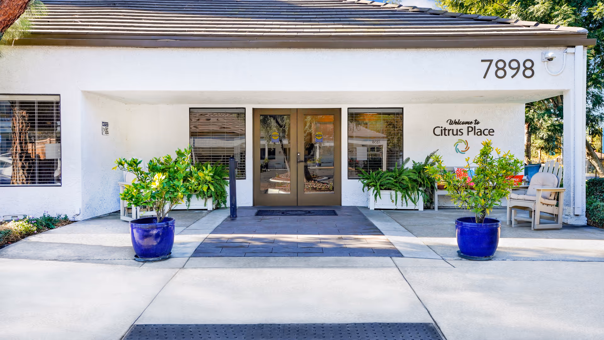 White facility entrance with Citrus Place sign, glass doors, and blue potted plants outside.