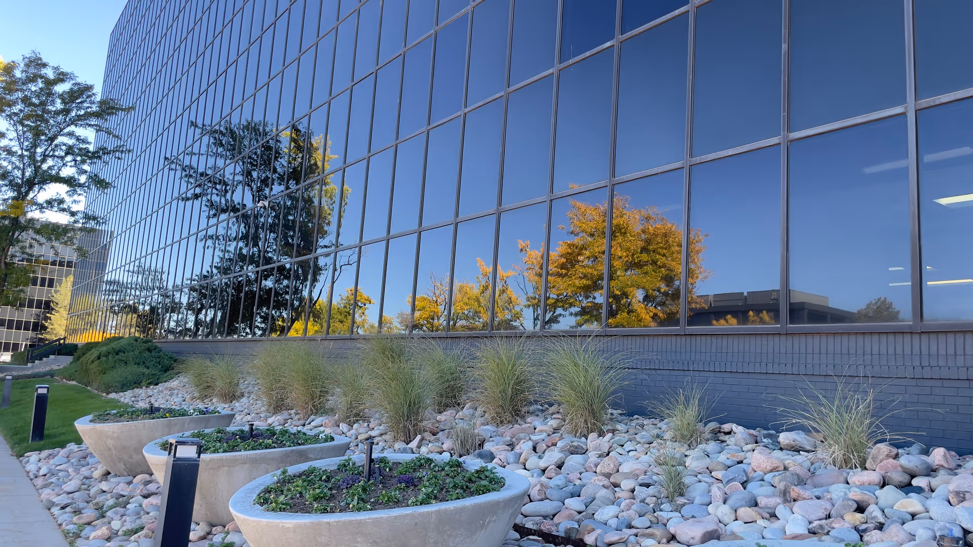 Modern glass-walled building exterior with rock landscaping and planters.