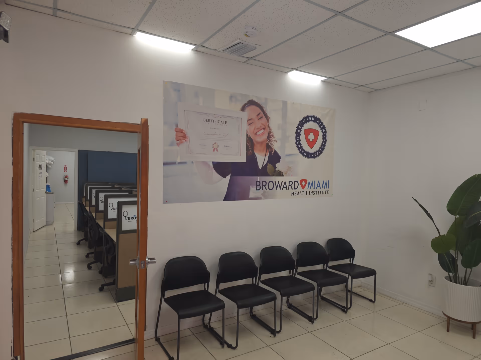 White-walled waiting area with six black chairs and a poster on the wall.