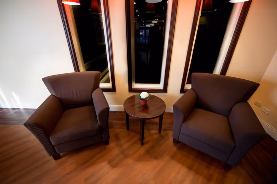 Two brown armchairs flank a round table with a plant in Crestwood Rehabilitation Ctr lounge.
