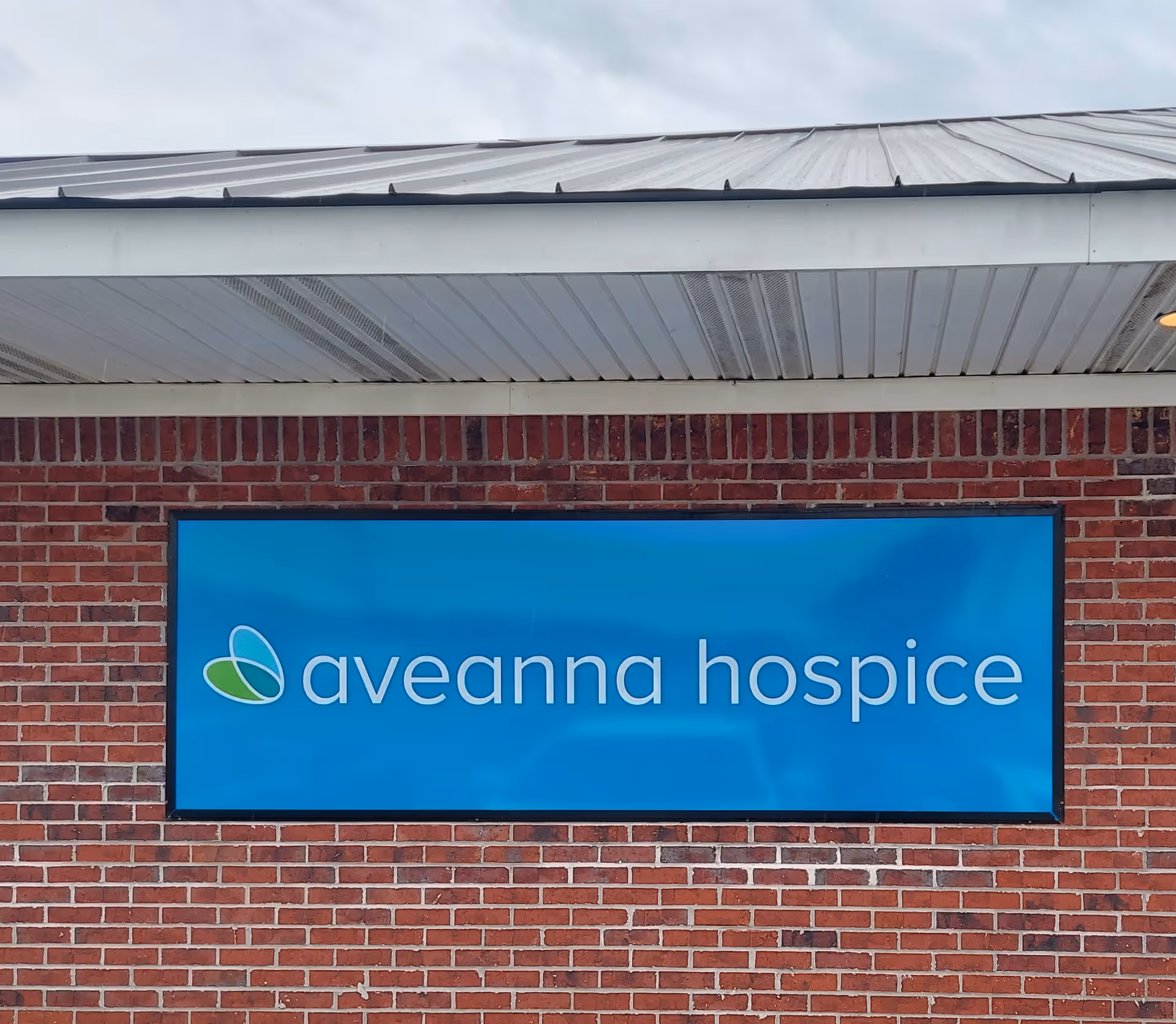 Blue Aveanna Hospice sign on a red brick building exterior
