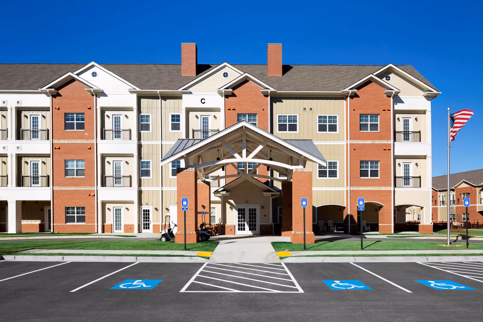 Front exterior of a multi-story senior living building with a covered entrance and accessible parking.