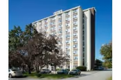 Tall multi-story senior living building with cars, trees, and a blue sky.