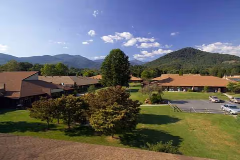 Wide view of low, brown-roofed senior living buildings with green lawns and mountains behind