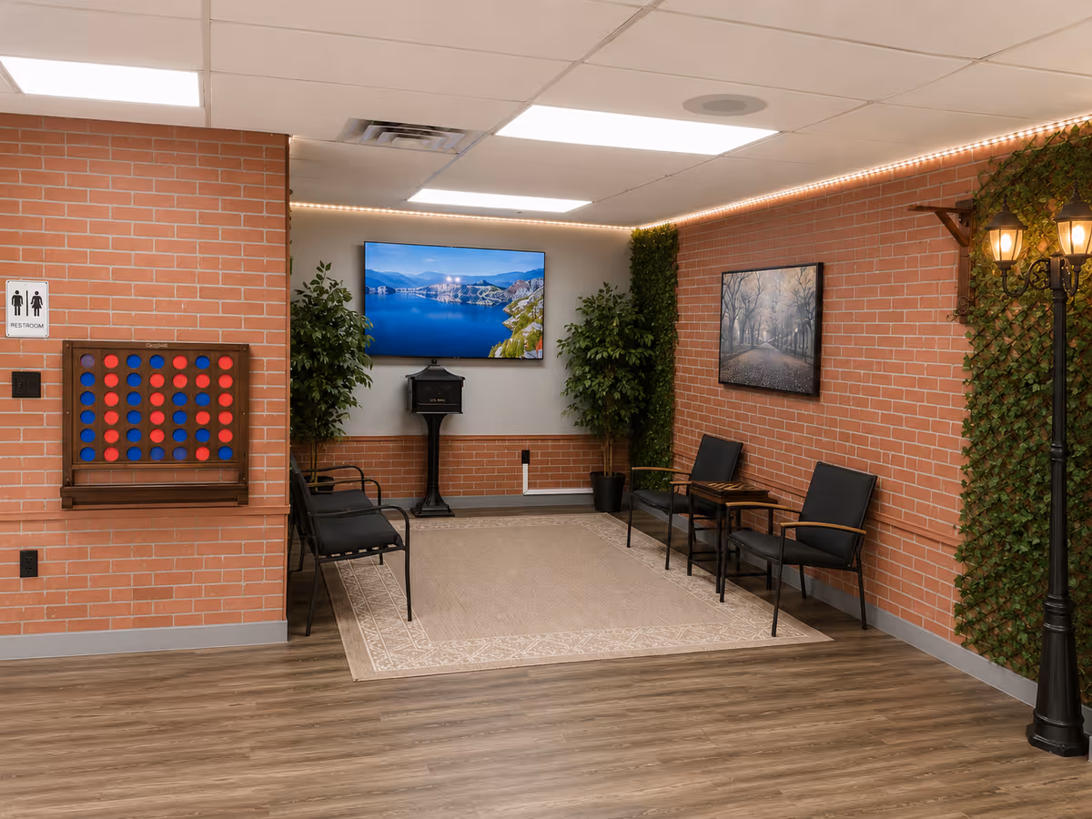 Indoor lobby with brick walls, rows of chairs, a TV screen, and decorative plants.