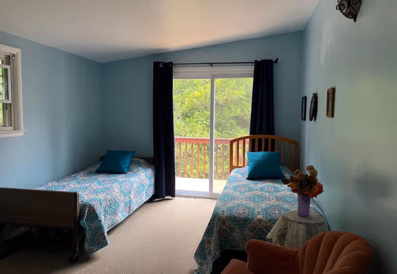 Two twin beds with teal pillows sit in a blue bedroom with a sliding balcony door.