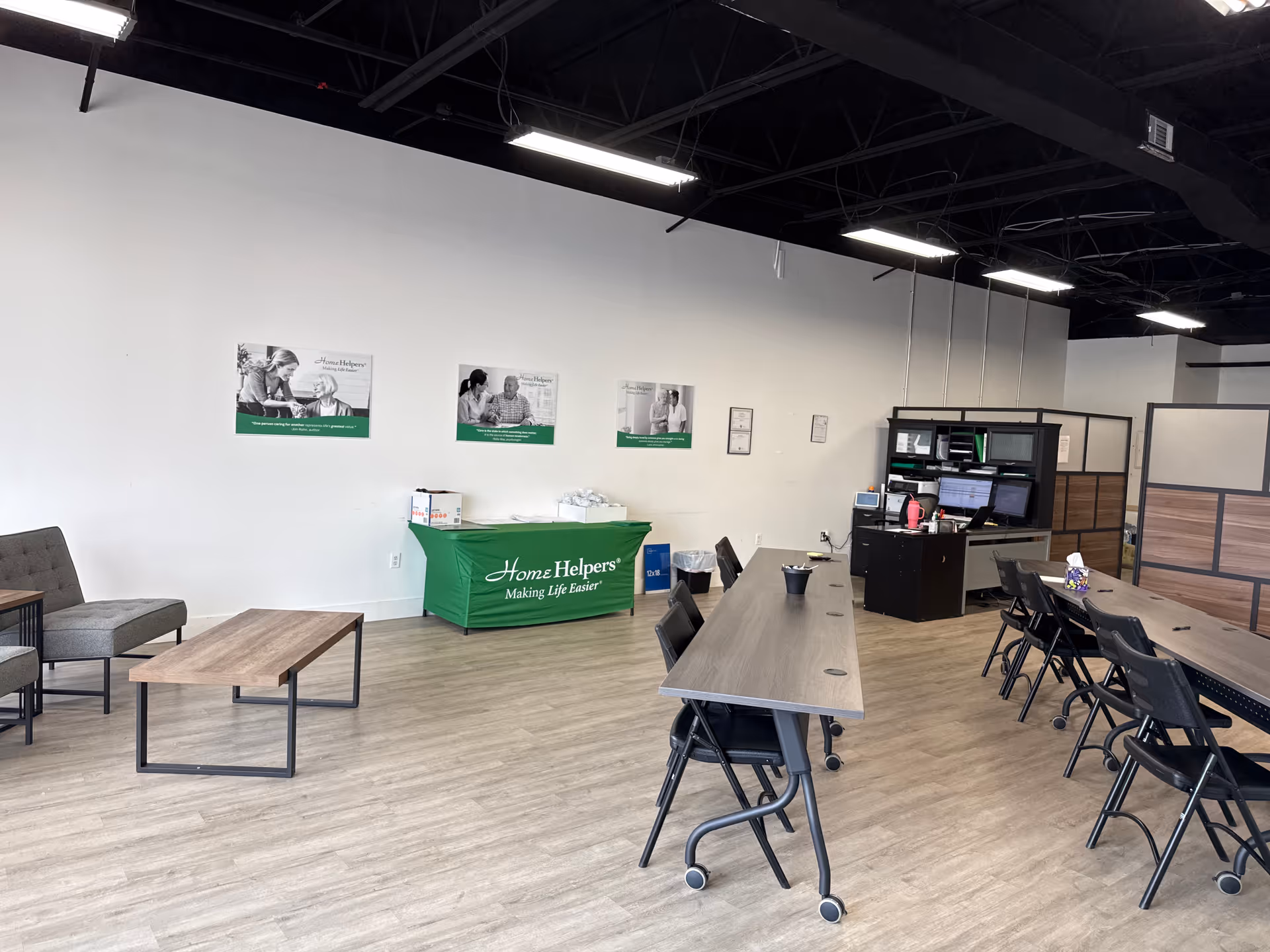 Interior office space with long tables, chairs, and a green Home Helpers banner.