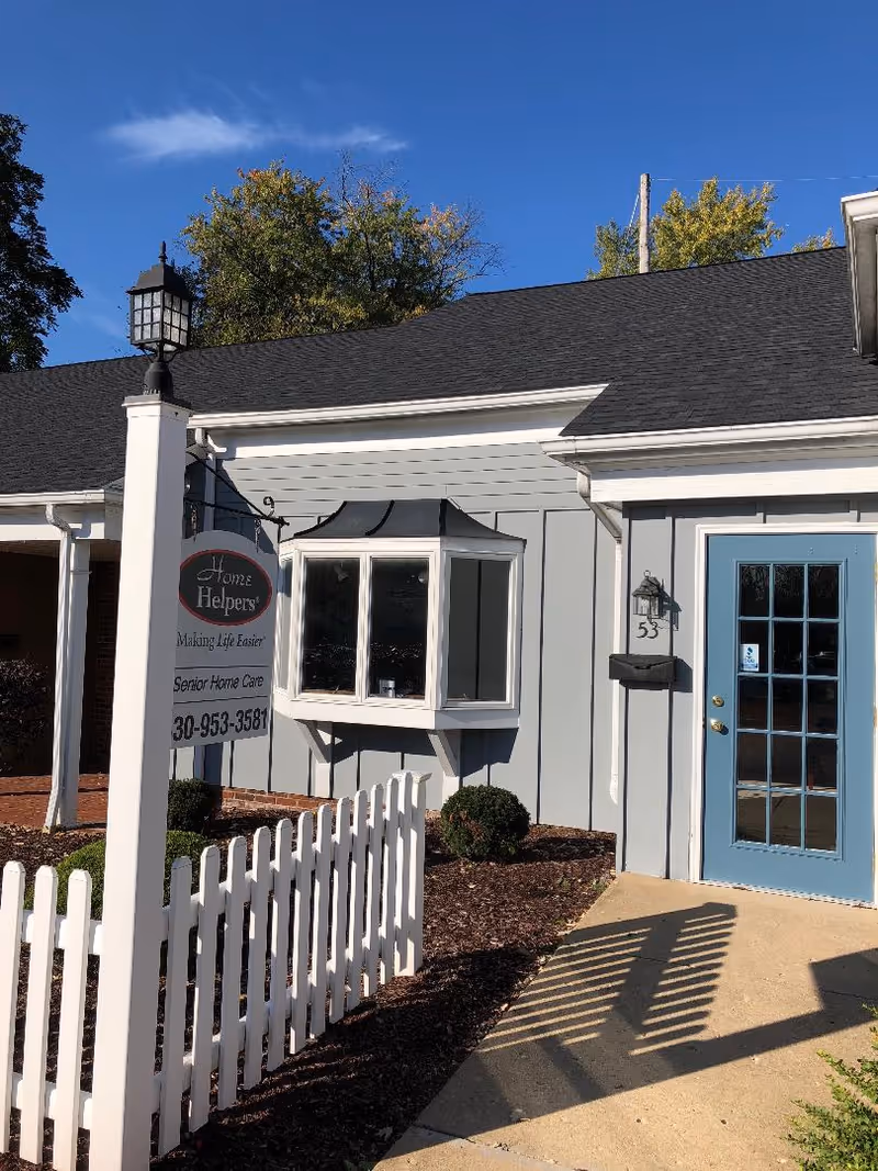 Exterior view of Home Helpers facility with blue door, sign, and white fence.