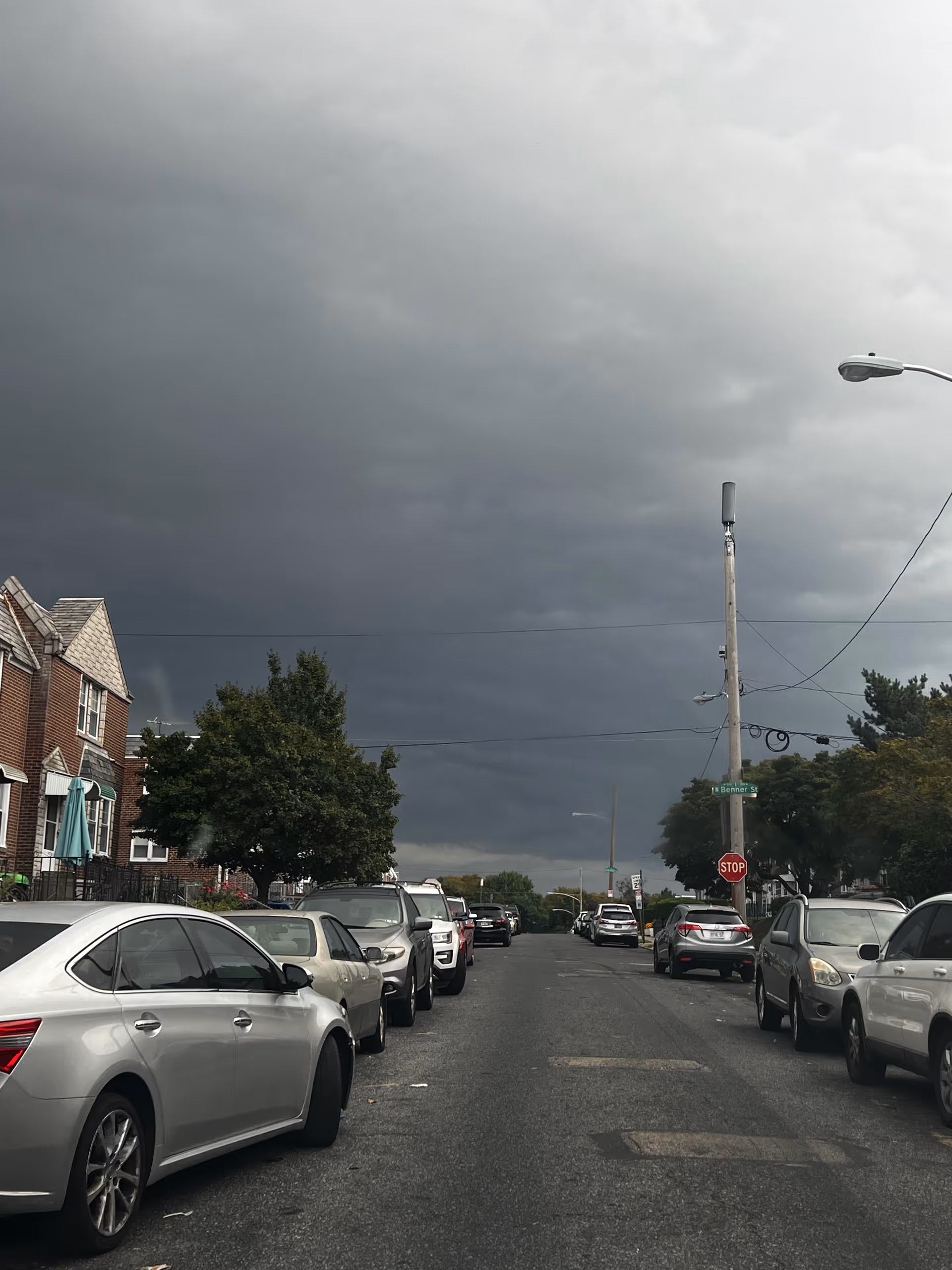 Stormy sky over a residential street lined with parked cars and brick houses.