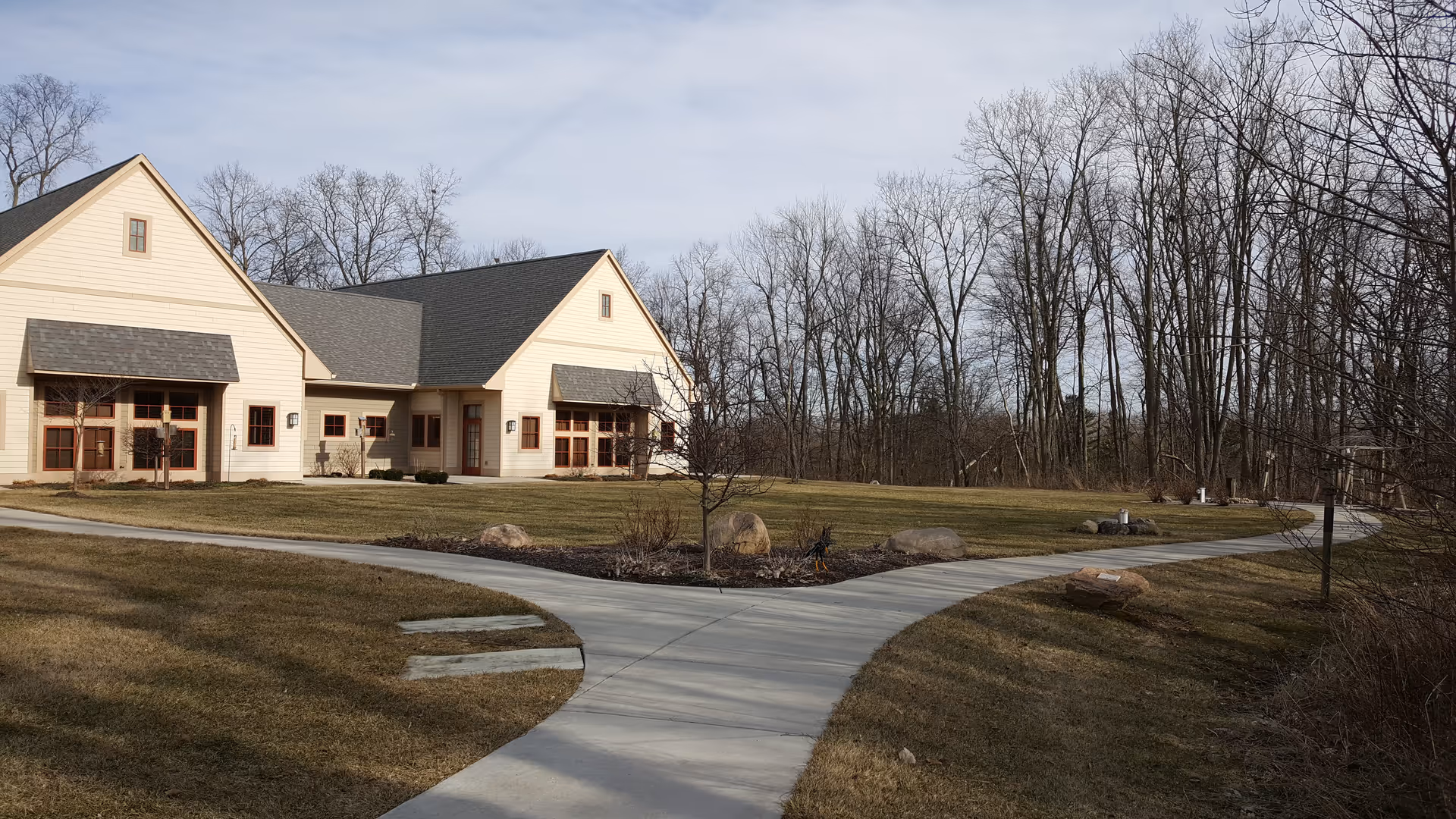 A light-colored hospice building's front with curved walkway and bare trees.