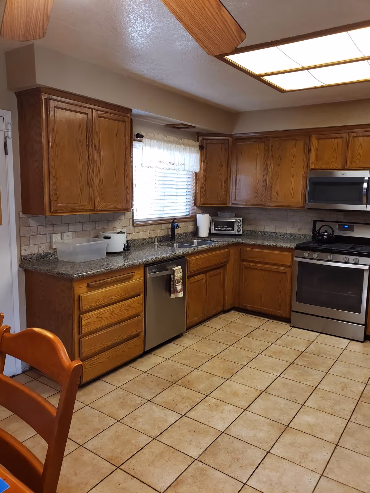U-shaped kitchen with wooden cabinets, granite counters, stainless appliances, and a window above the sink.
