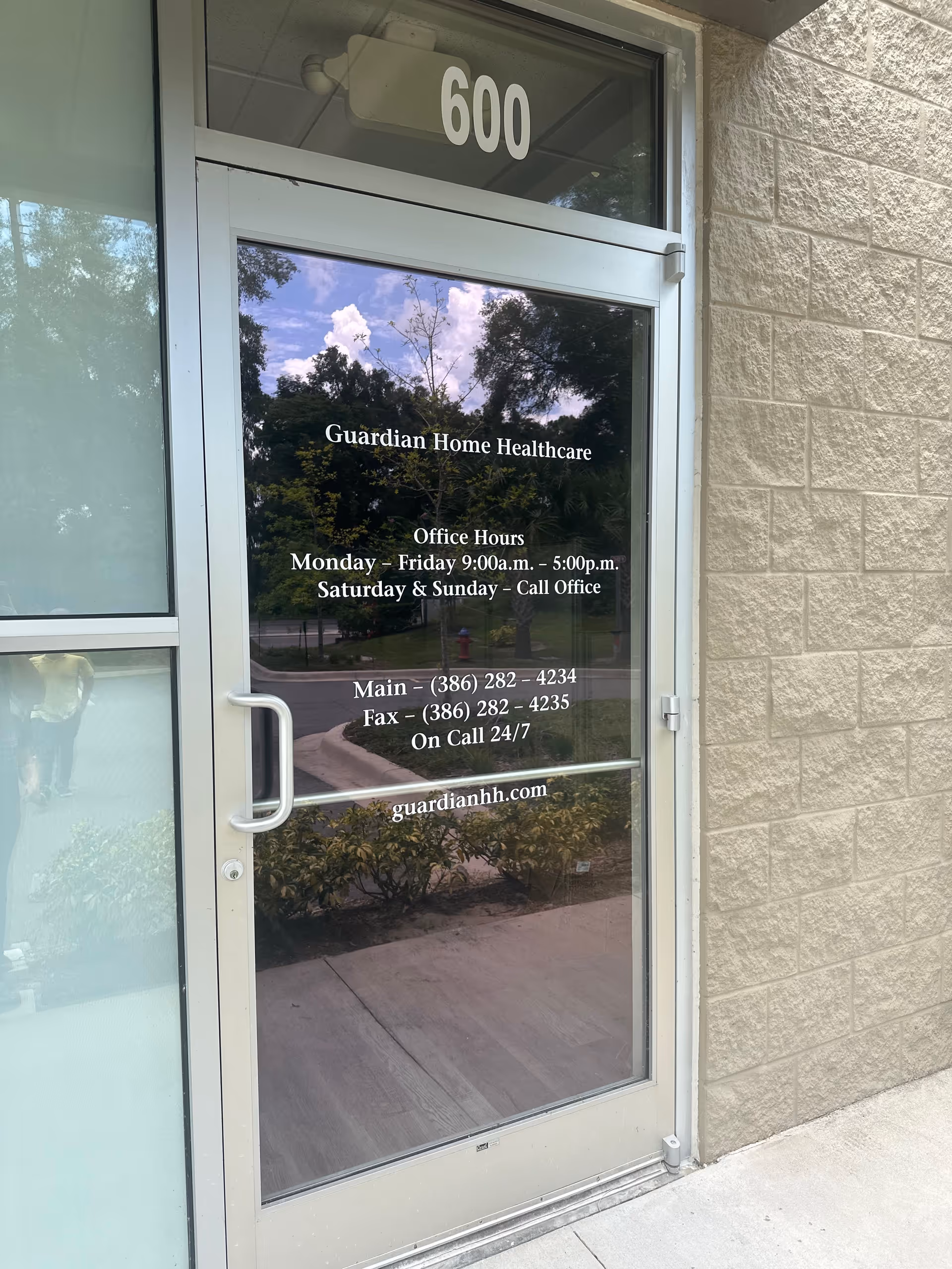 Glass door of Guardian Home Healthcare with hours and contact info on the building front.