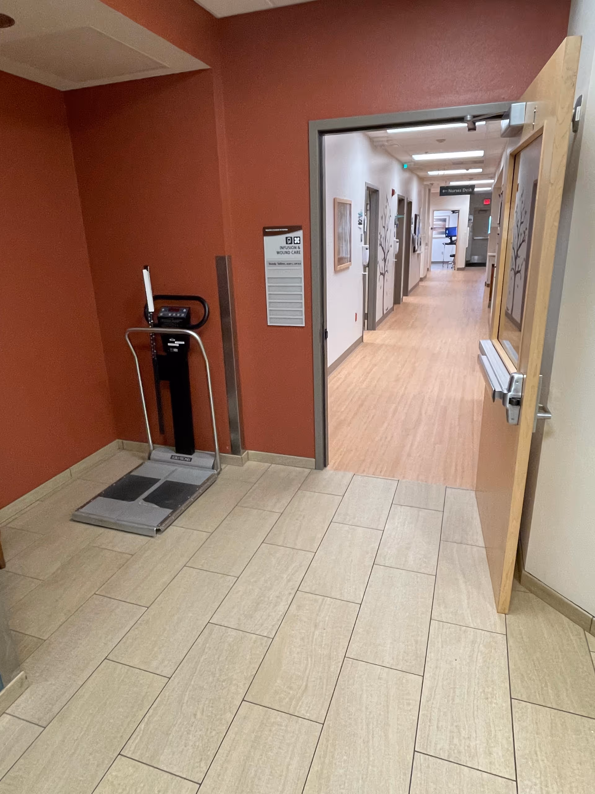 Indoor corridor with red walls, a weighing scale, and open doorway to a long hallway.