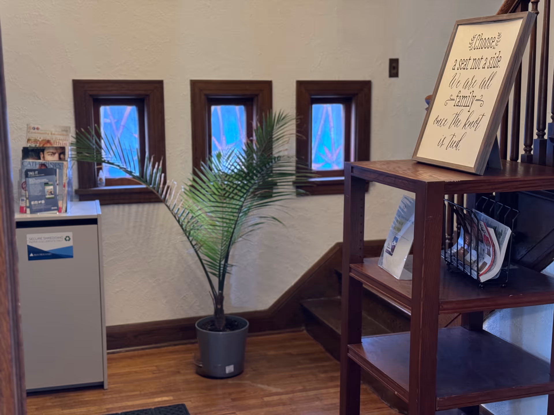 Indoor lobby area with a potted plant, magazines, and a framed wall quote.