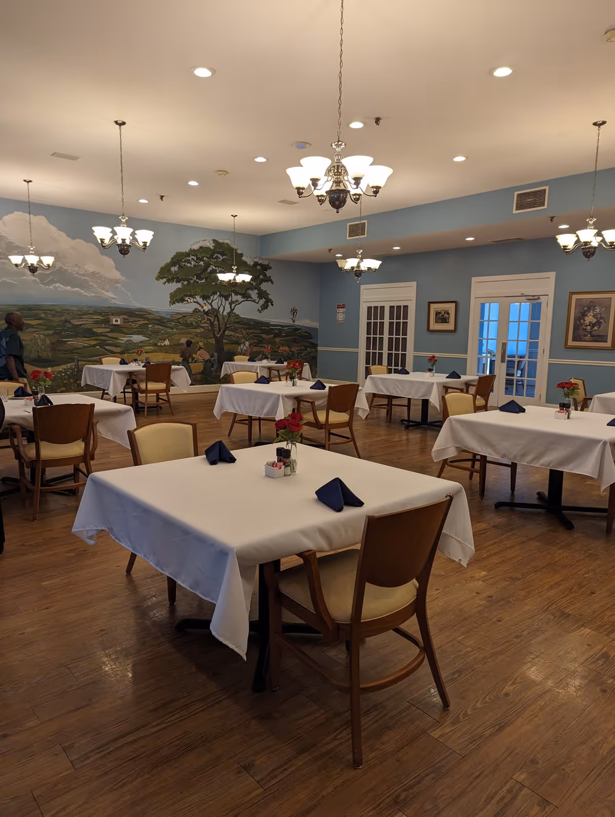 Dining room in Sagepoint Senior Living Services with white-tablecloth tables and chandeliers.