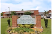 Exterior view of Obion County Nursing Home with a brick sign and landscaped yard.