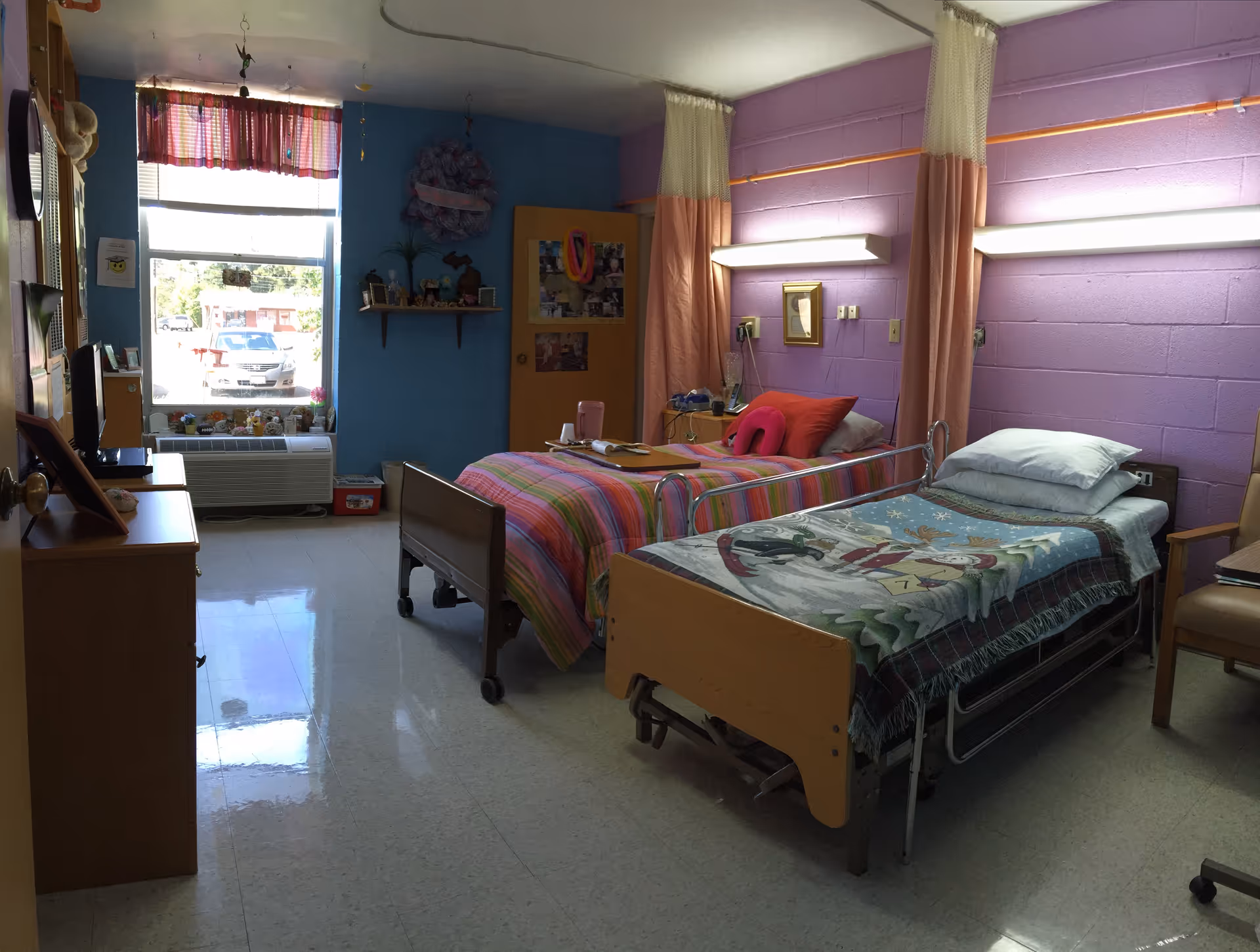 Two single beds with colorful blankets in a bright, shared bedroom at a senior facility.