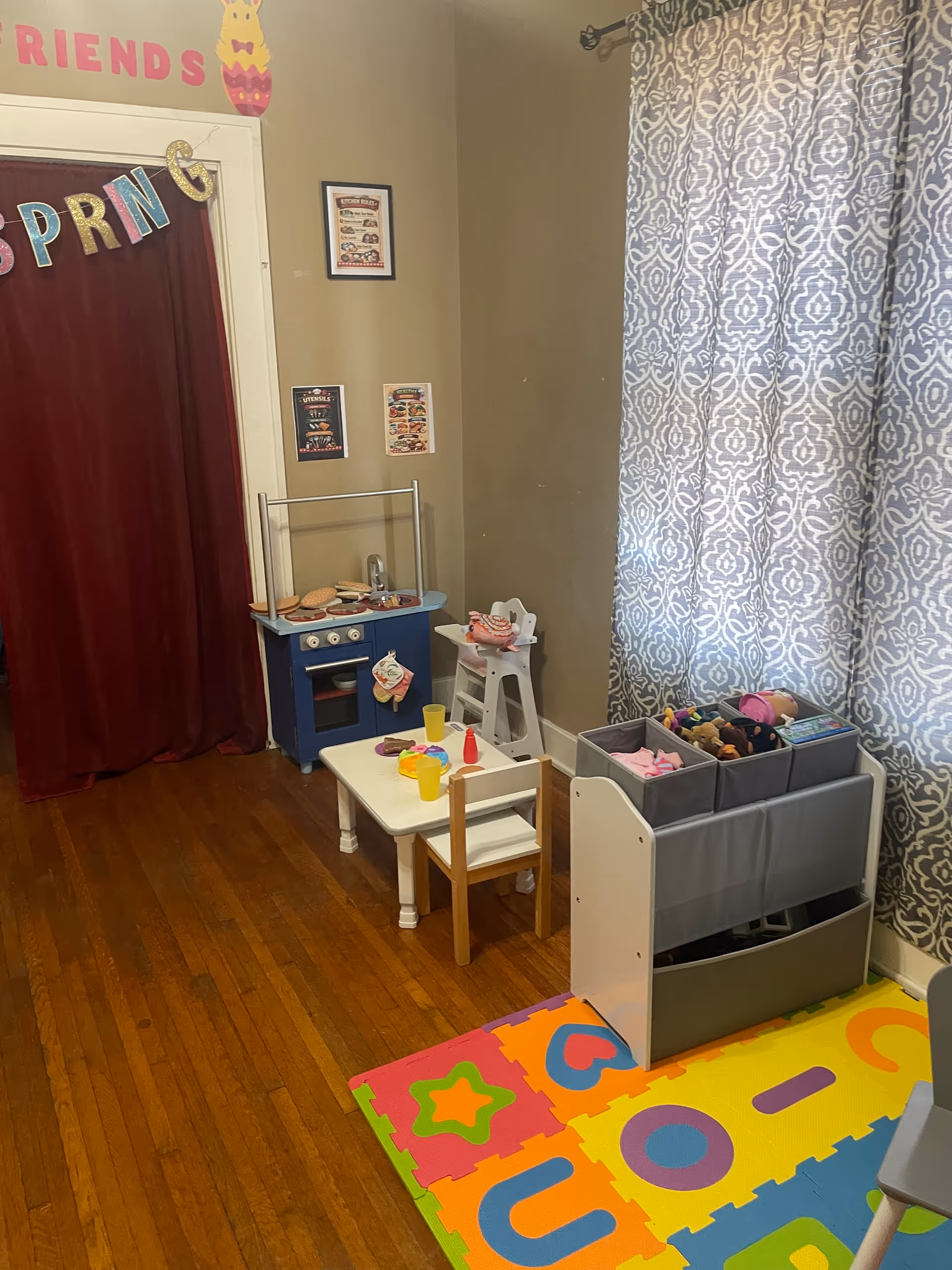 Indoor playroom in a senior facility with toy kitchen, table, storage, and colorful mat.