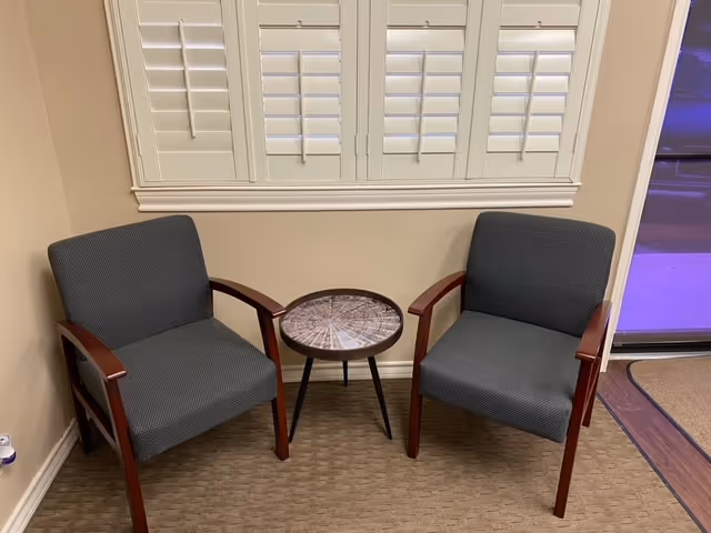 Two gray chairs flank a small round table in a beige-walled interior seating area.
