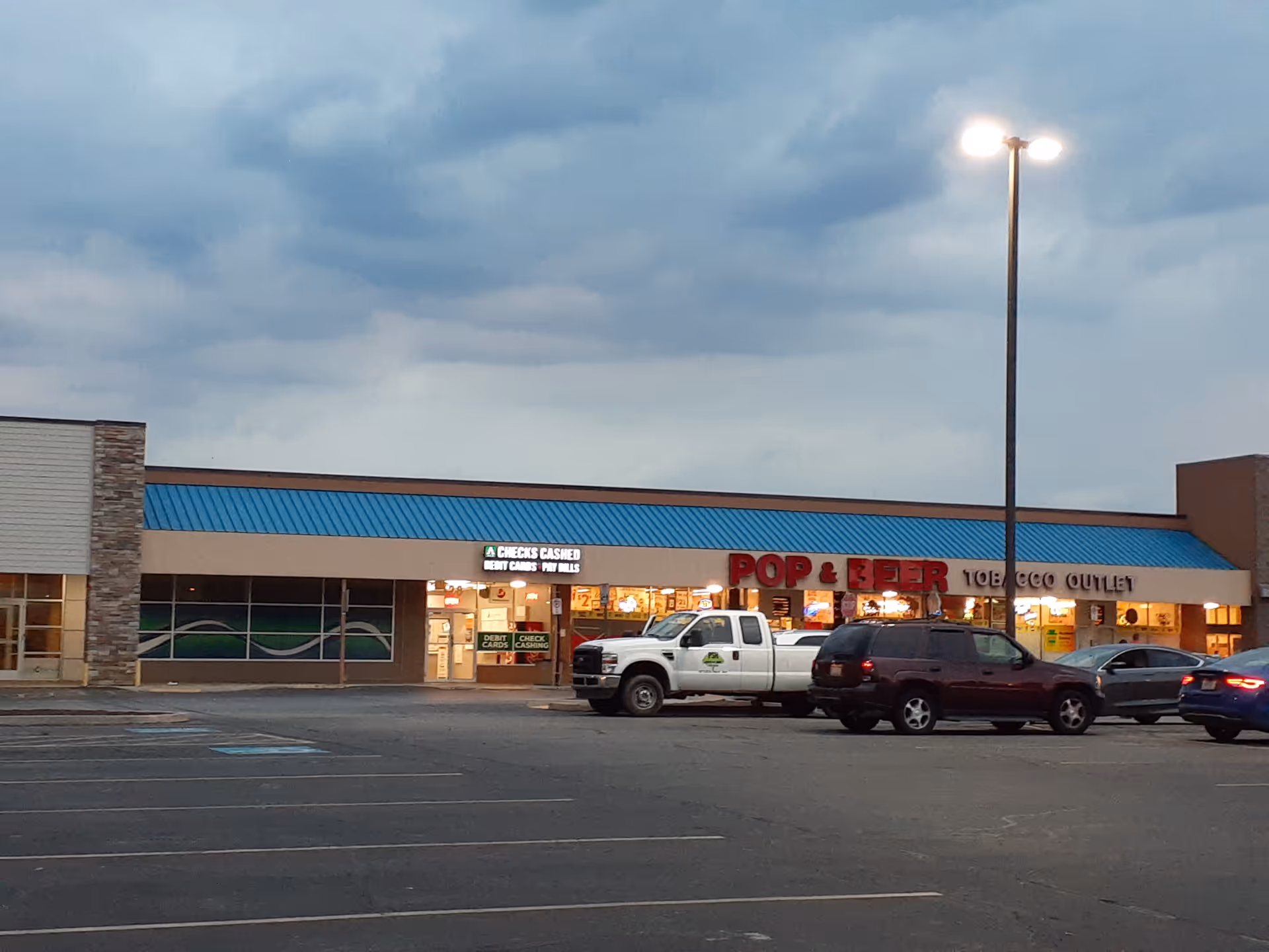 Exterior view of strip mall storefronts with a parking lot and streetlamps.