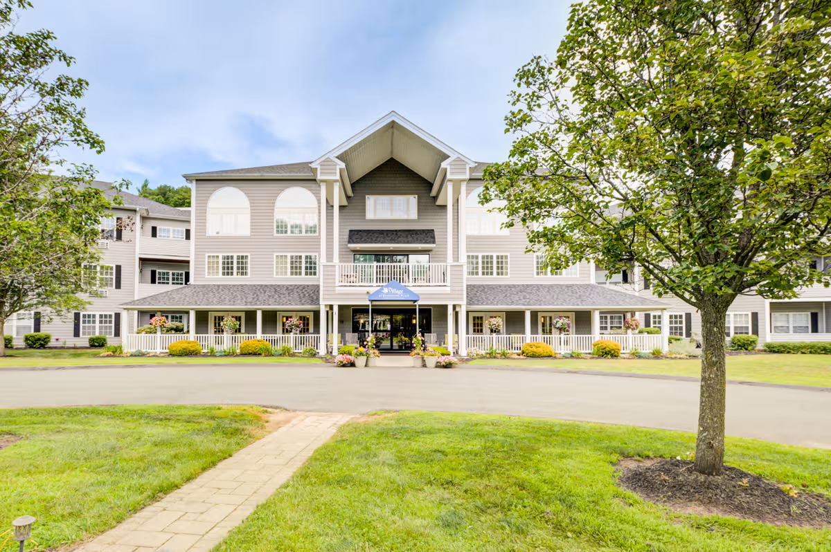 Front view of a gray senior living facility with a welcoming entrance and greenery.
