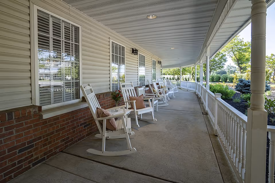 Covered front porch with white rocking chairs along a railing overlooking landscaped grounds.