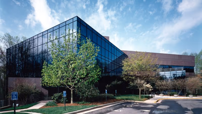 Modern glass-front senior living facility building with trees and a parking lot.
