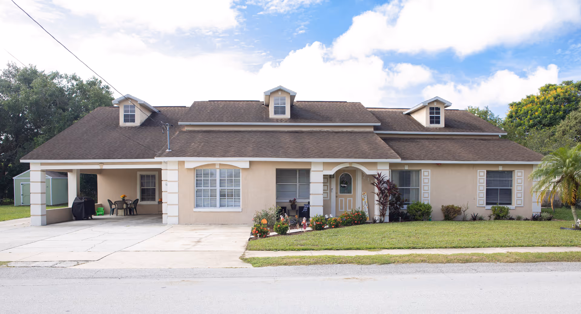 Front exterior of a single-story beige suburban house with a carport, driveway, front lawn and small garden.