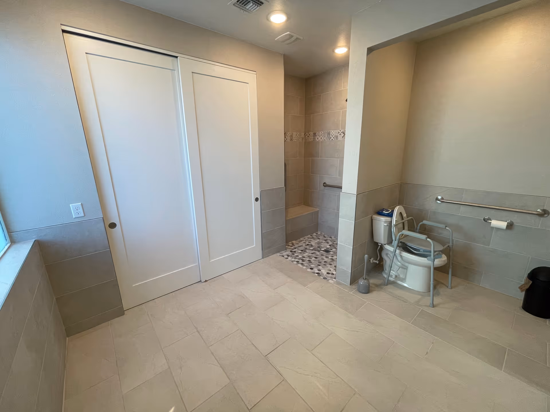 Accessible bathroom featuring a shower stall, toilet with grab bars, and a transfer chair.
