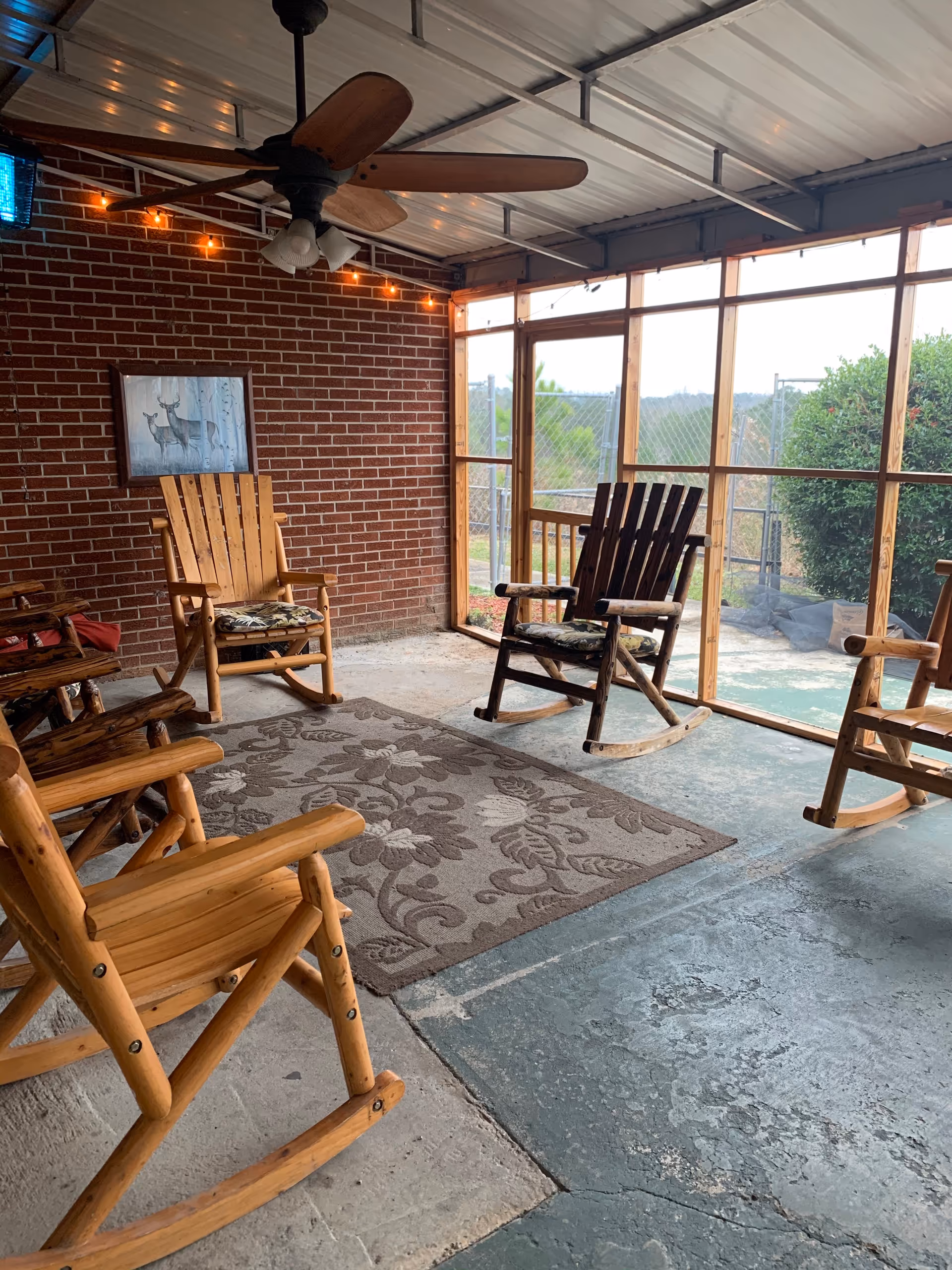 Wooden rocking chairs surround a rug on a screened brick patio with string lights.