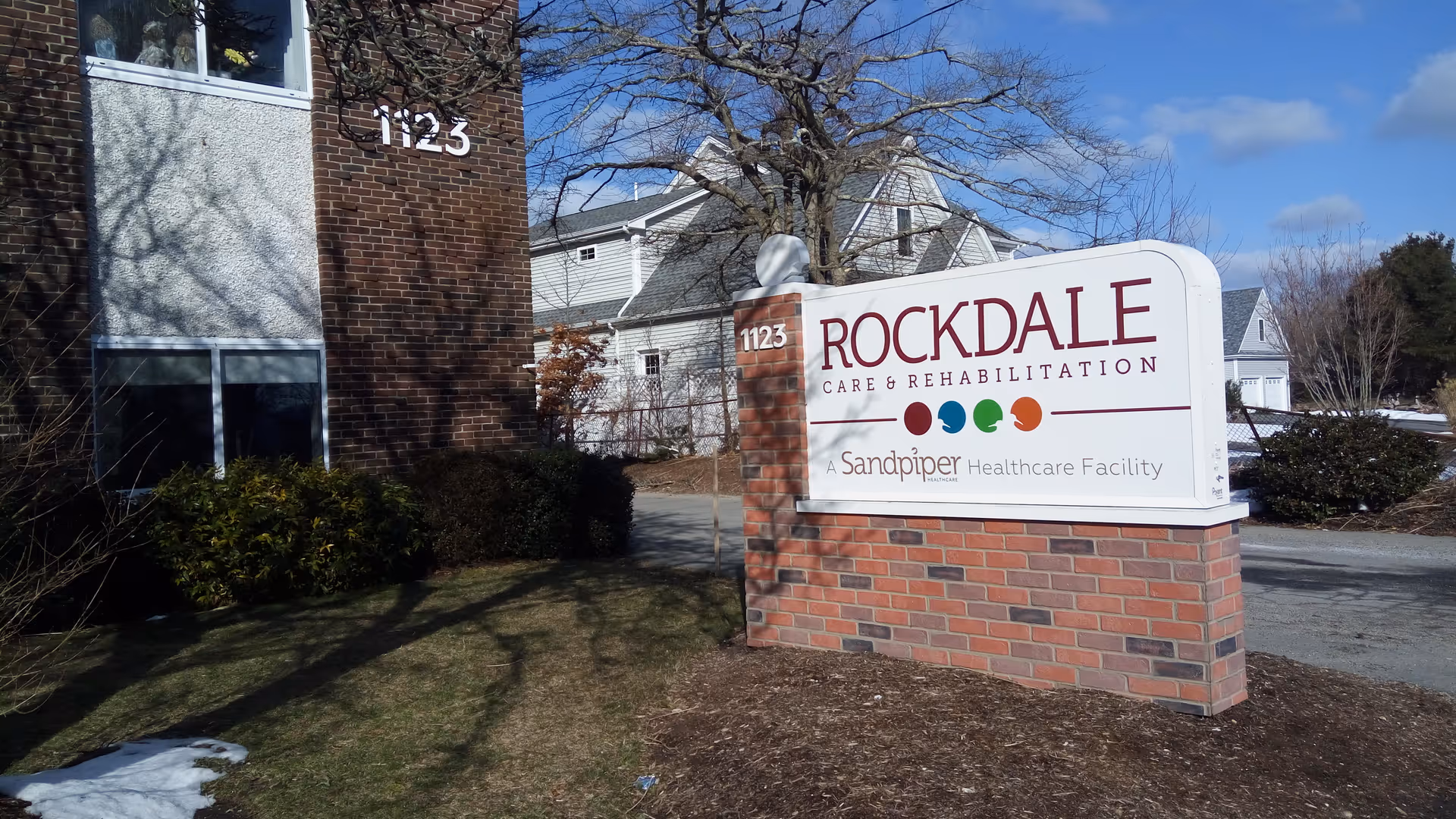 Outdoor sign for Rockdale Care and Rehabilitation in front of brick building.