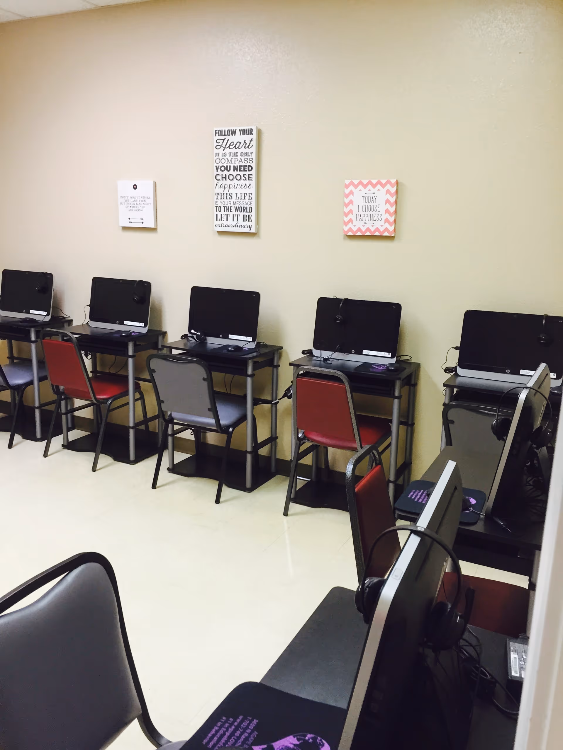 Row of computer stations with monitors and chairs along a beige wall.