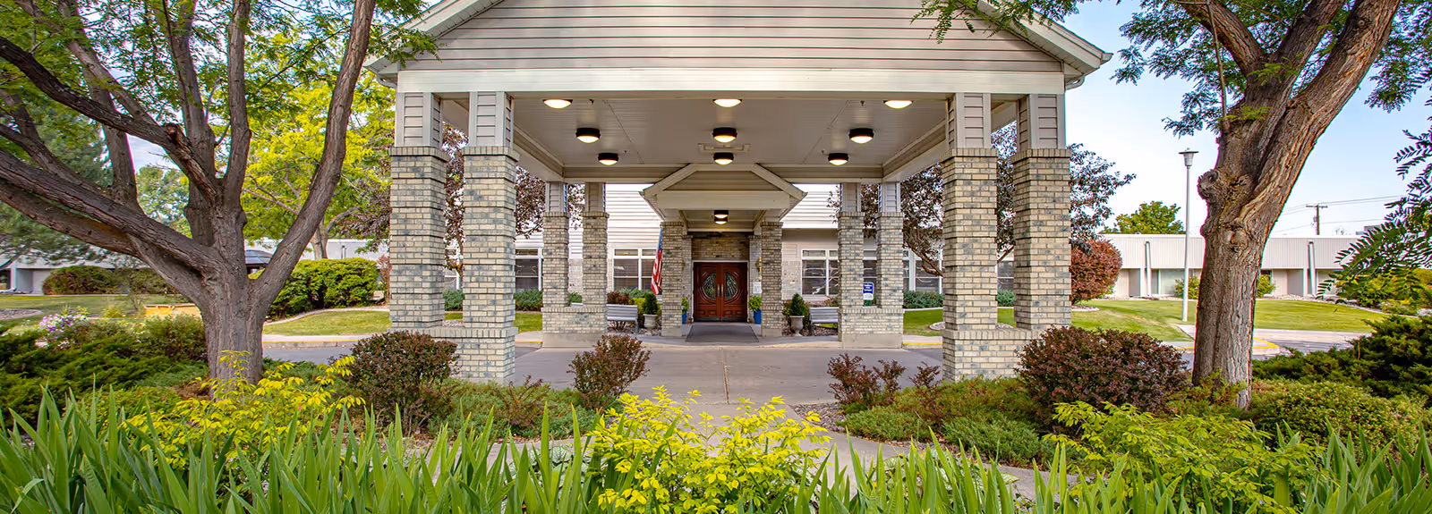 Covered main entrance with a porte-cochere supported by brick columns, framed by trees and landscaped greenery.