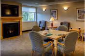 Cozy senior living lounge with a fireplace, windows, and four upholstered chairs around a table.