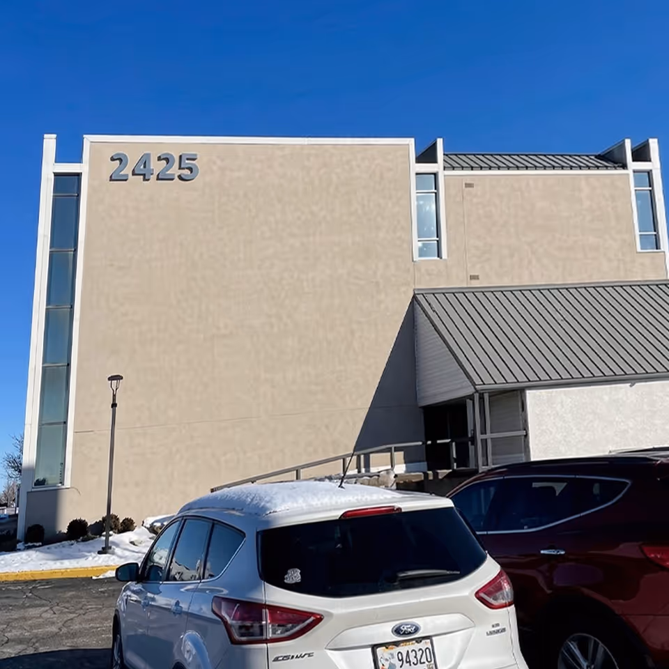 Front exterior of a beige facility with the number 2425 and parked cars.