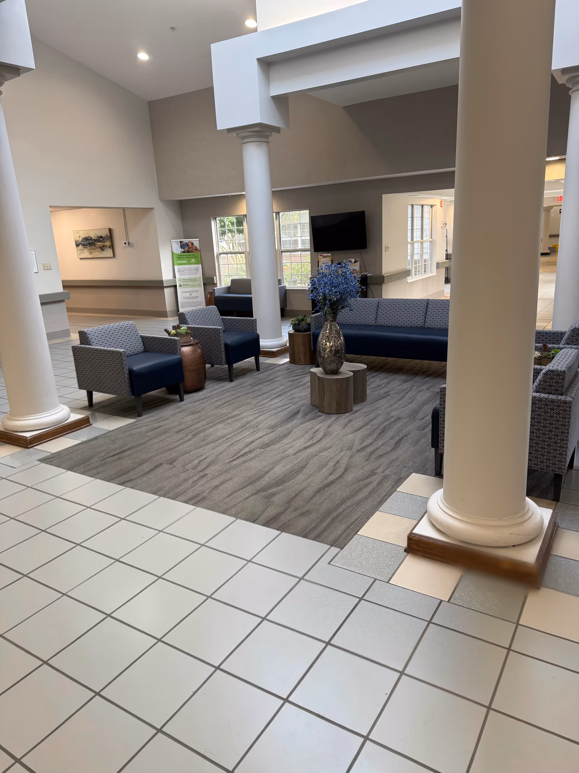 Senior living facility lobby with columns, seating, and a wall-mounted TV.