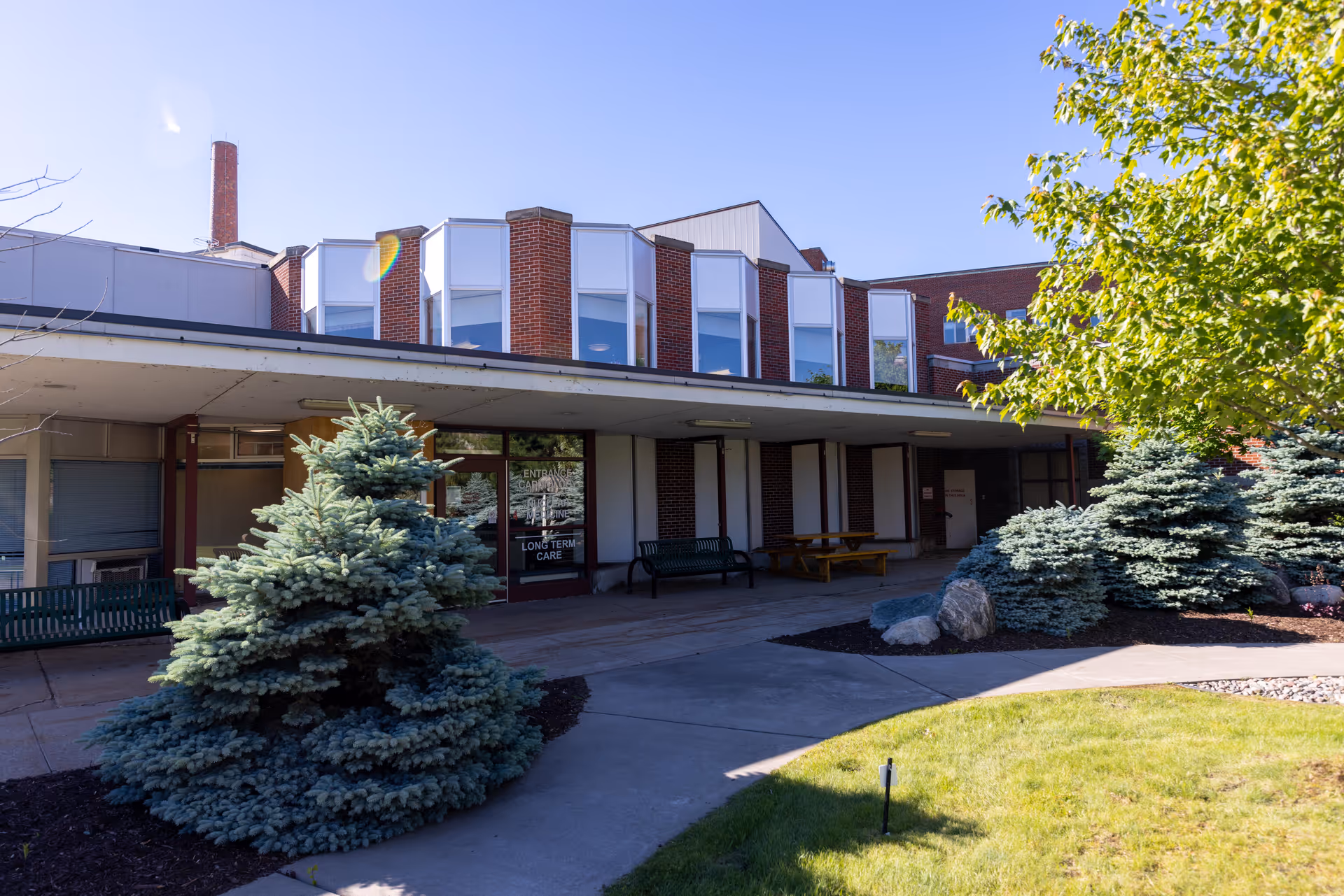 Exterior view of a brick facility entrance with benches and landscaped shrubs.