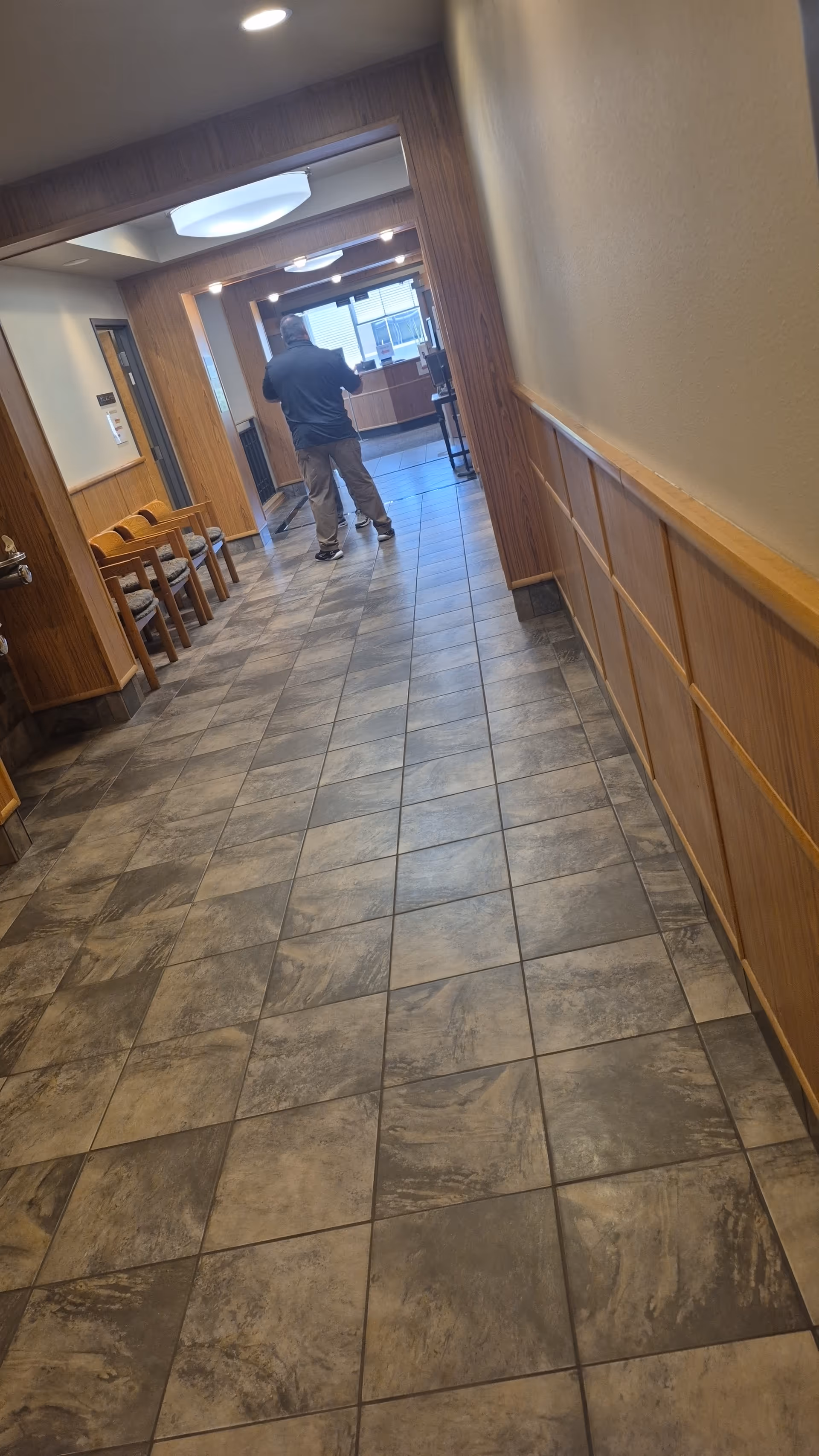 A long tiled hallway in a senior living facility with wood paneling and chairs.
