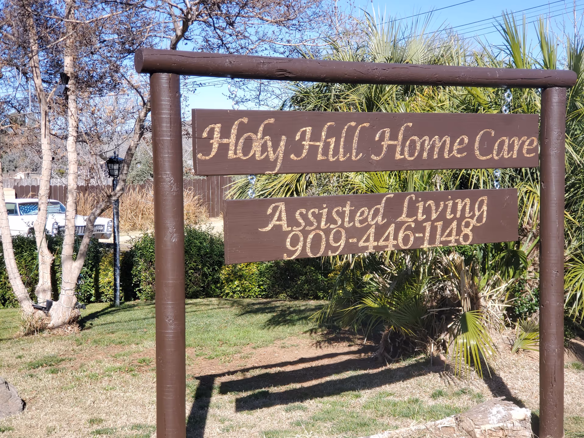 Wooden sign reading Holy Hill Home Care Assisted Living in a grassy outdoor area.