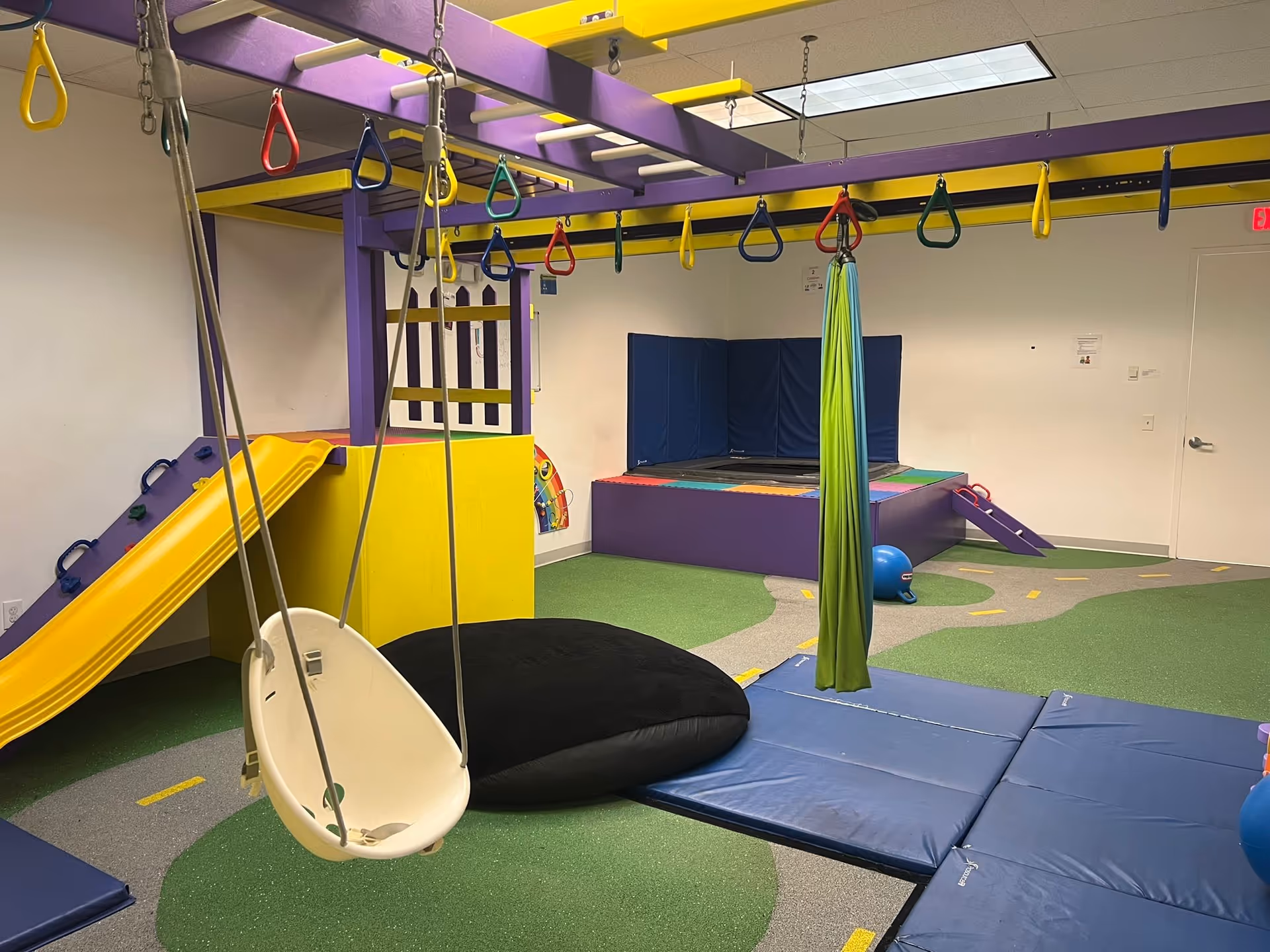 Colorful indoor therapy playroom with swings, padded mats, and climbing structures.