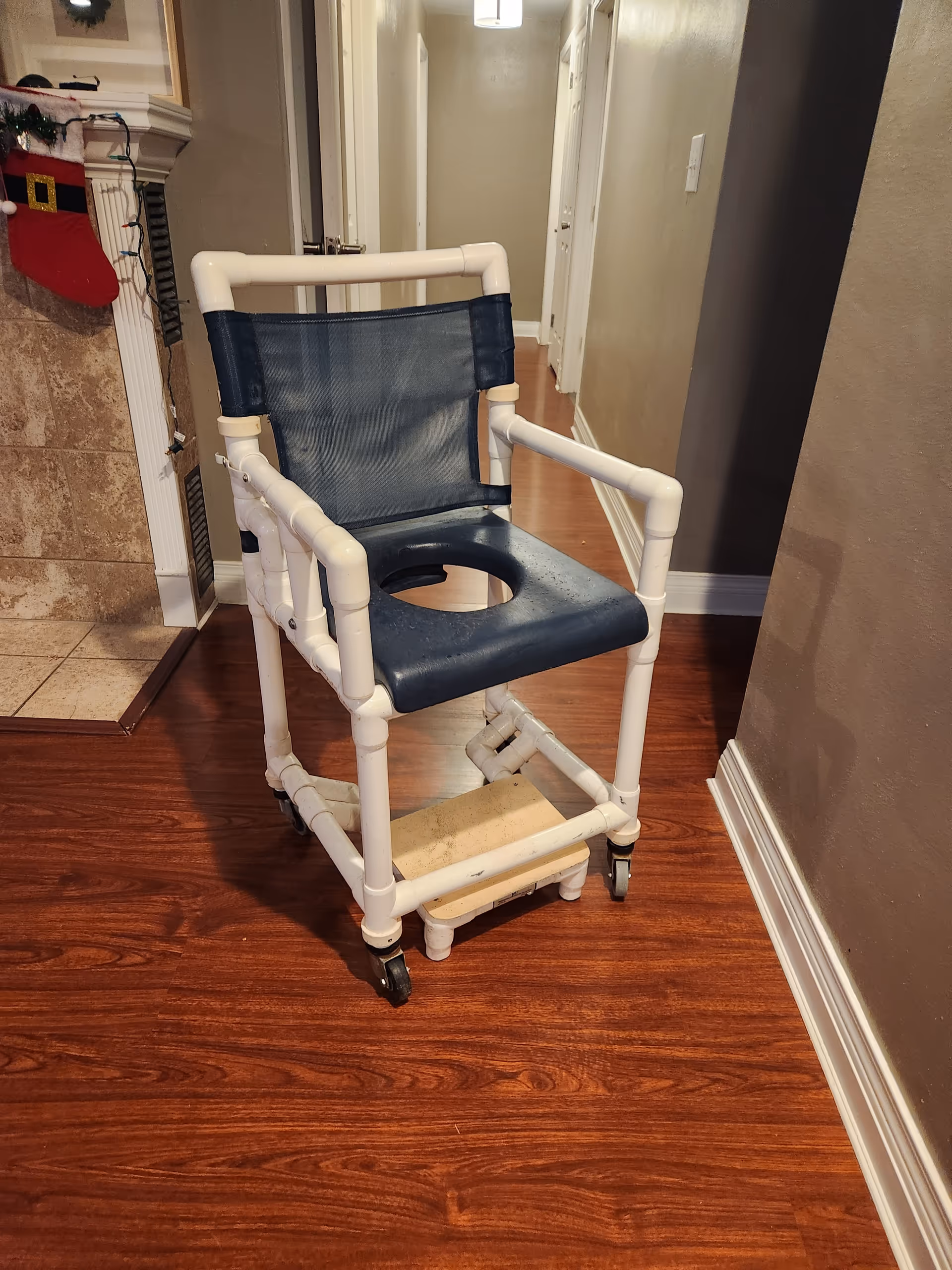 A blue and white rolling commode chair sits in a hallway near a fireplace.
