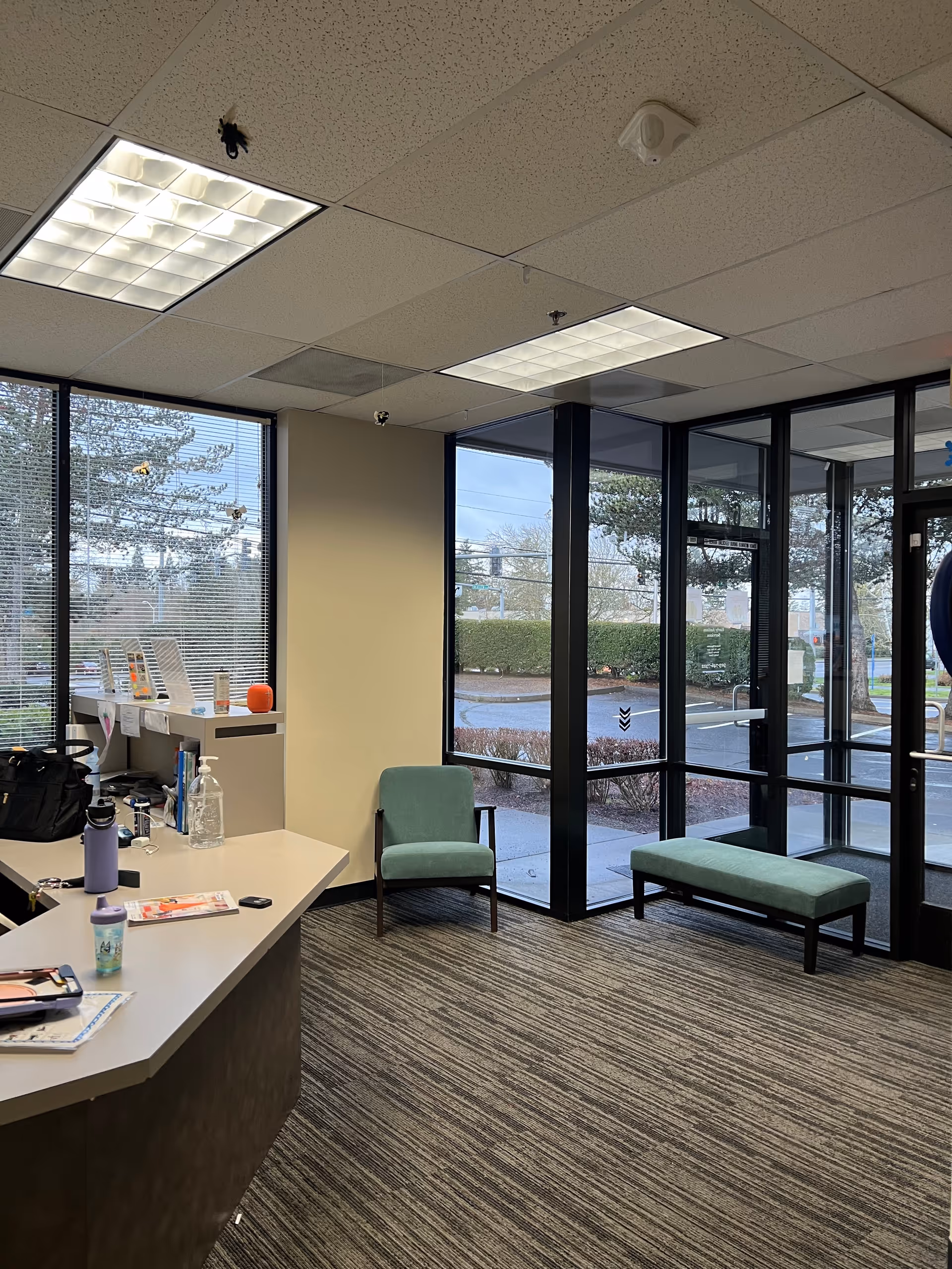 A reception lobby with teal chairs, a curved counter, and glass entrance doors.