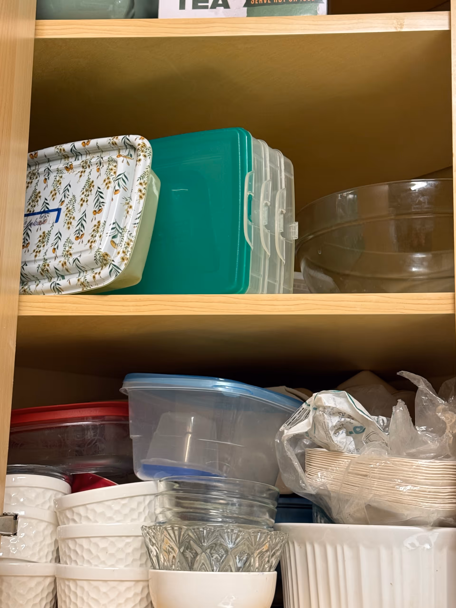 Open kitchen cabinet displaying stacked bowls, plastic containers, lids, and dishware.