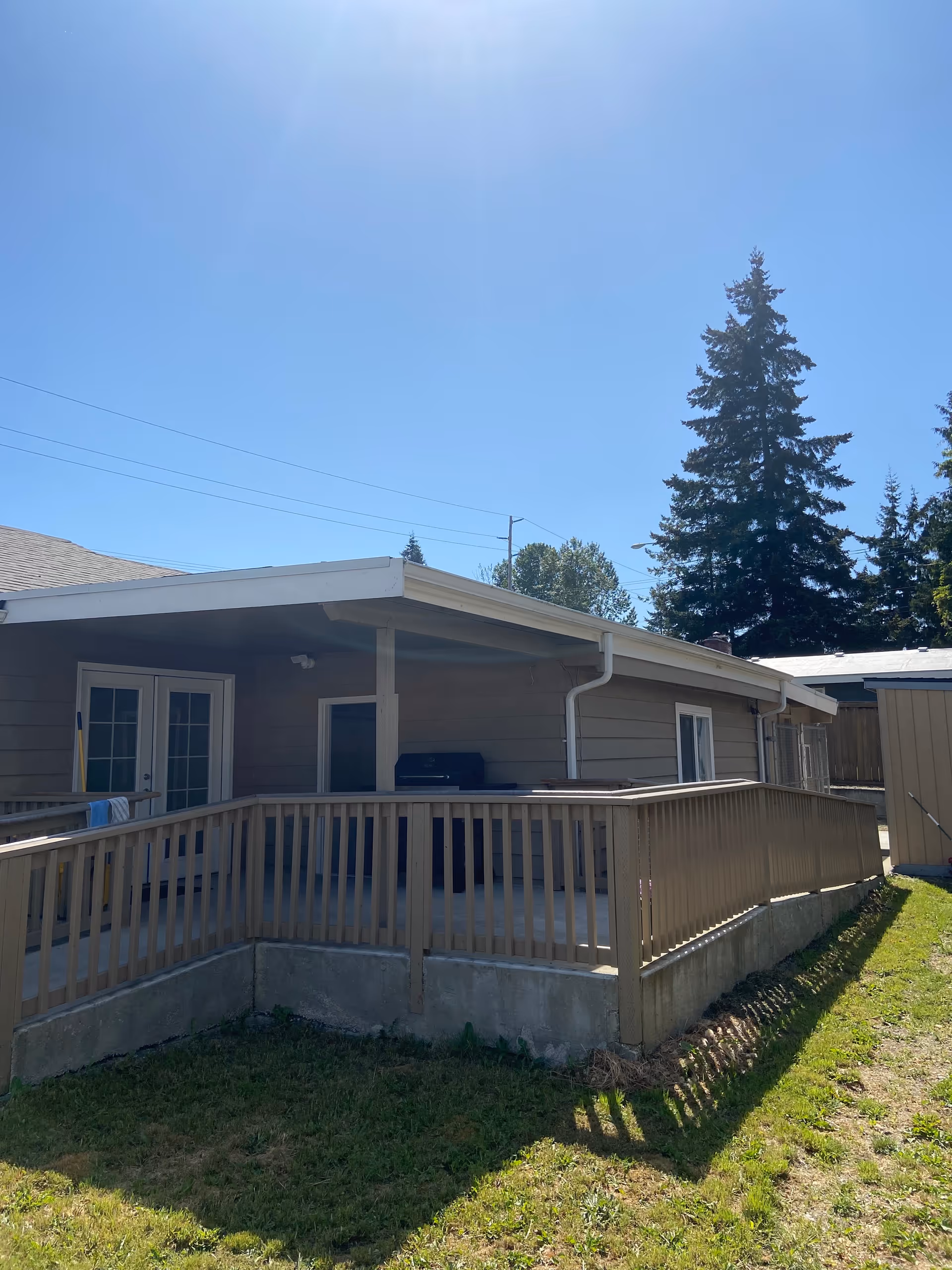 Single-story facility with a wooden deck, railing, and grill on a sunny day.