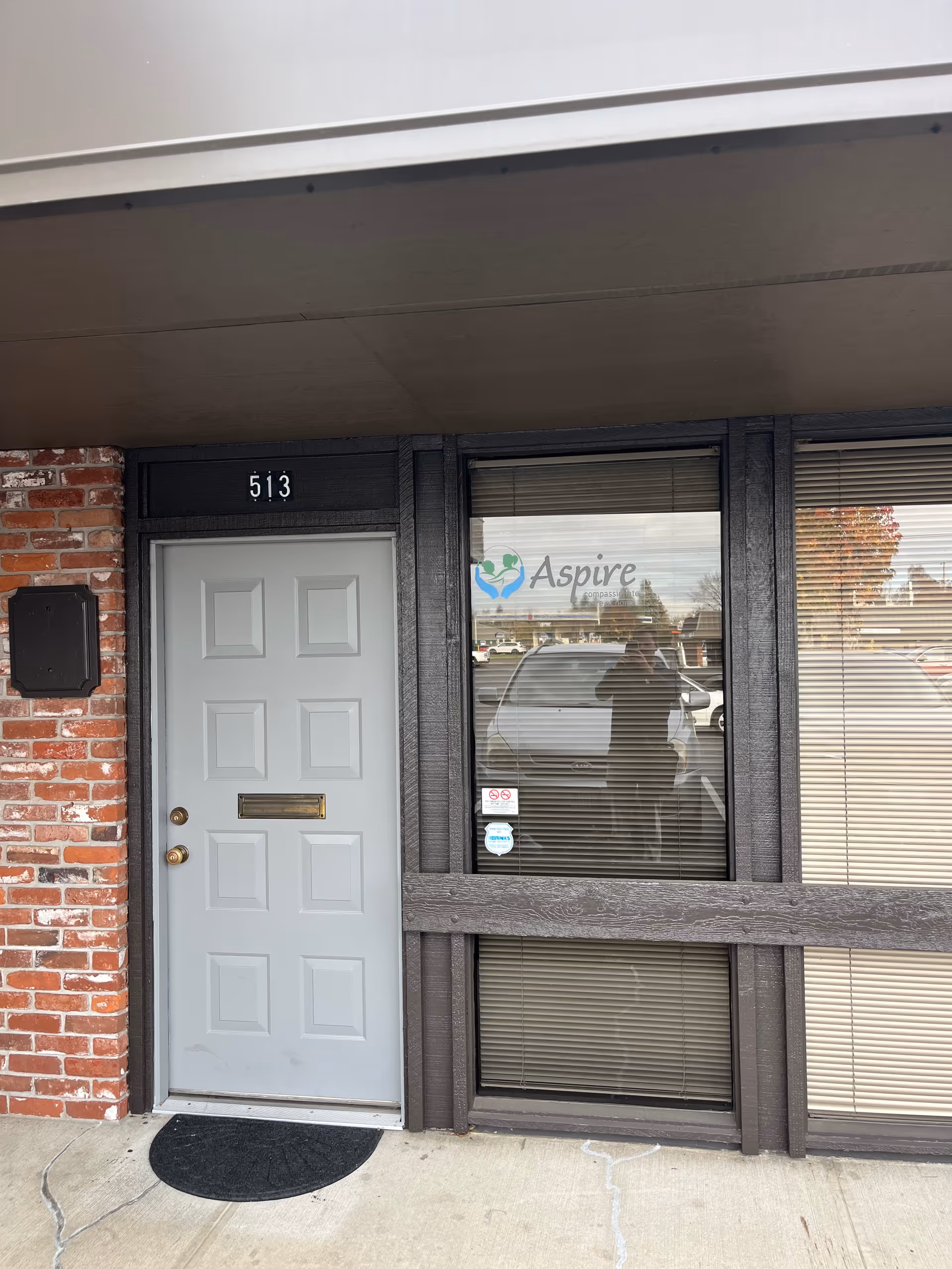 Grey front door beside a window displaying the Aspire Caregiving logo on a brick storefront.