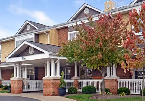 Front exterior of a brick senior living facility with a covered entrance and trees.