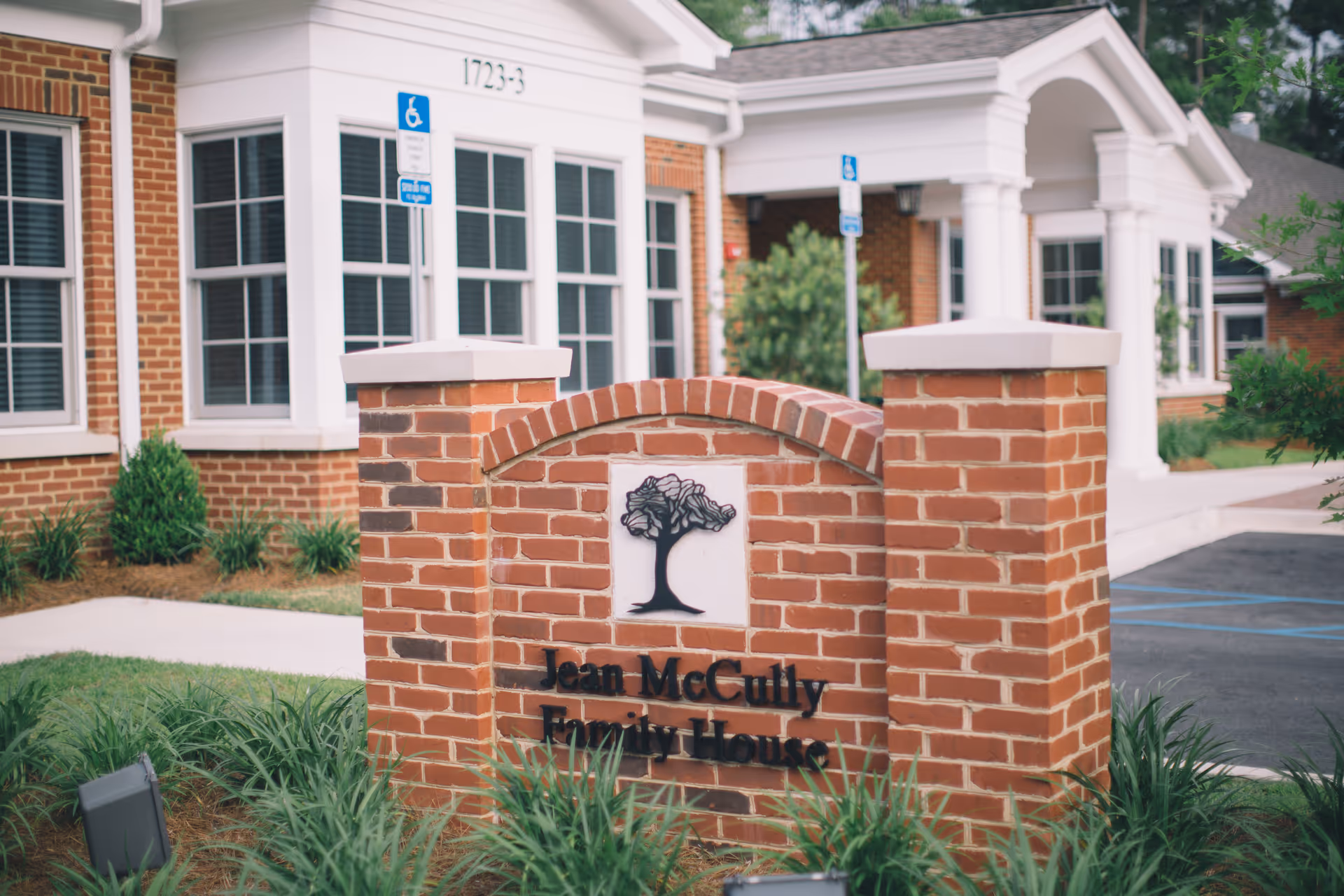 Brick sign with tree emblem in front of a white-columned hospice building.