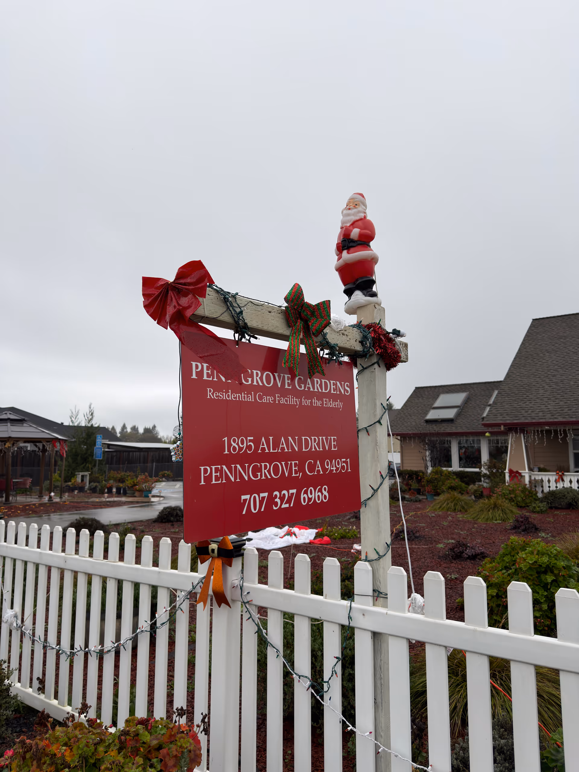 Red Penngrove Gardens sign on a wooden post with Christmas decorations and white picket fence